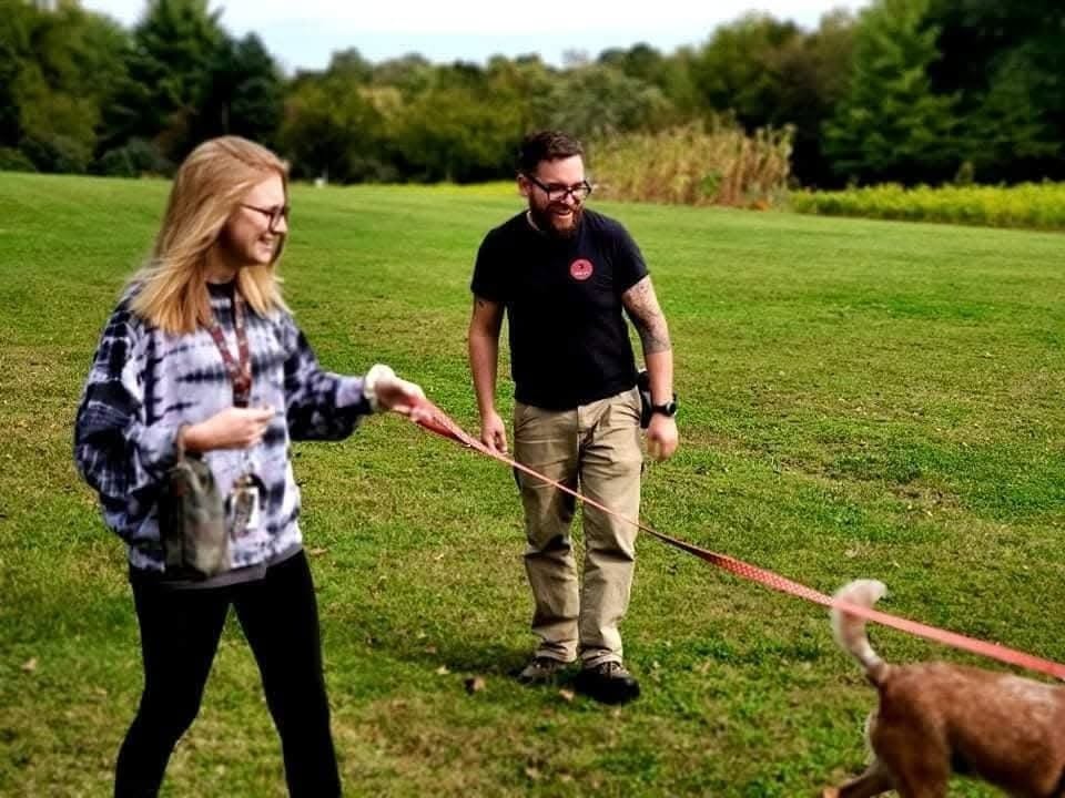 Ben laughing with a client in a field as she works her dog on a long lead